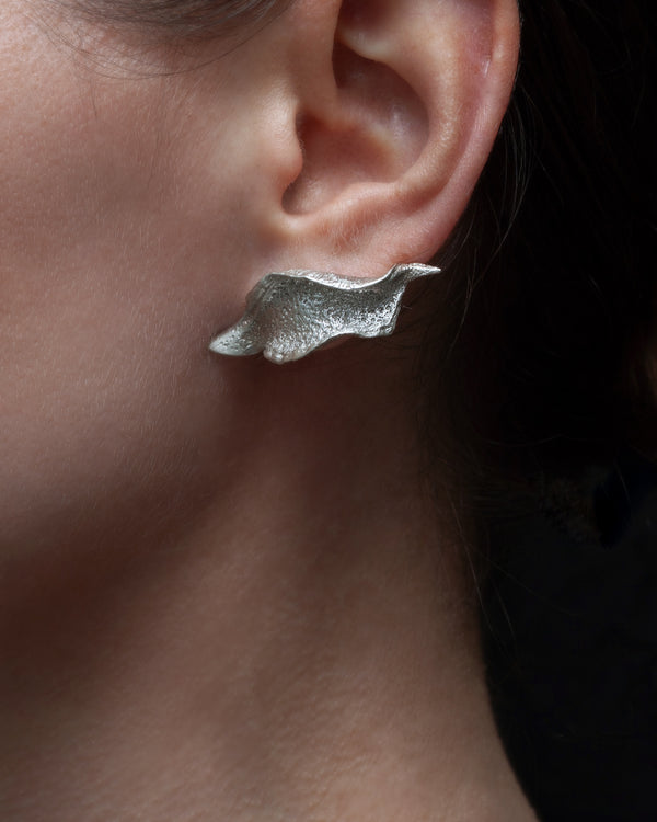 Close-up of a person wearing a silver wave-shaped earring.