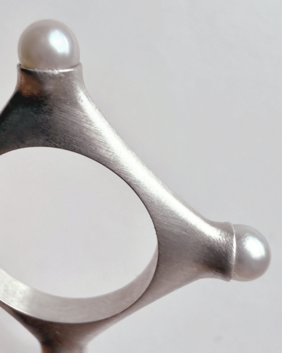 Fragment of geometric Argentium silver ring on a light gray background with fresh water pearls
