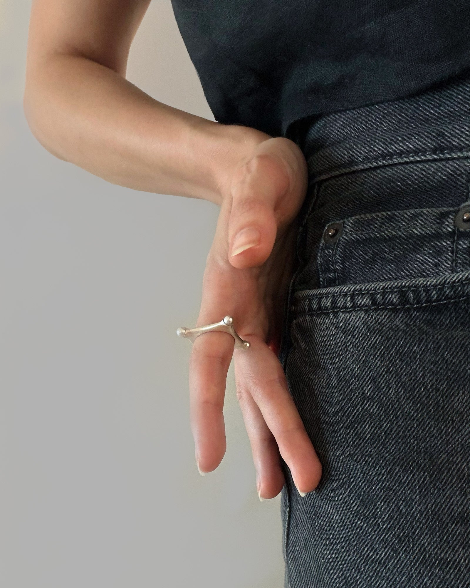 A close-up of a person's hand wearing a Argentium silver ring with fresh water pearls, resting against their dark denim jeans and black top.