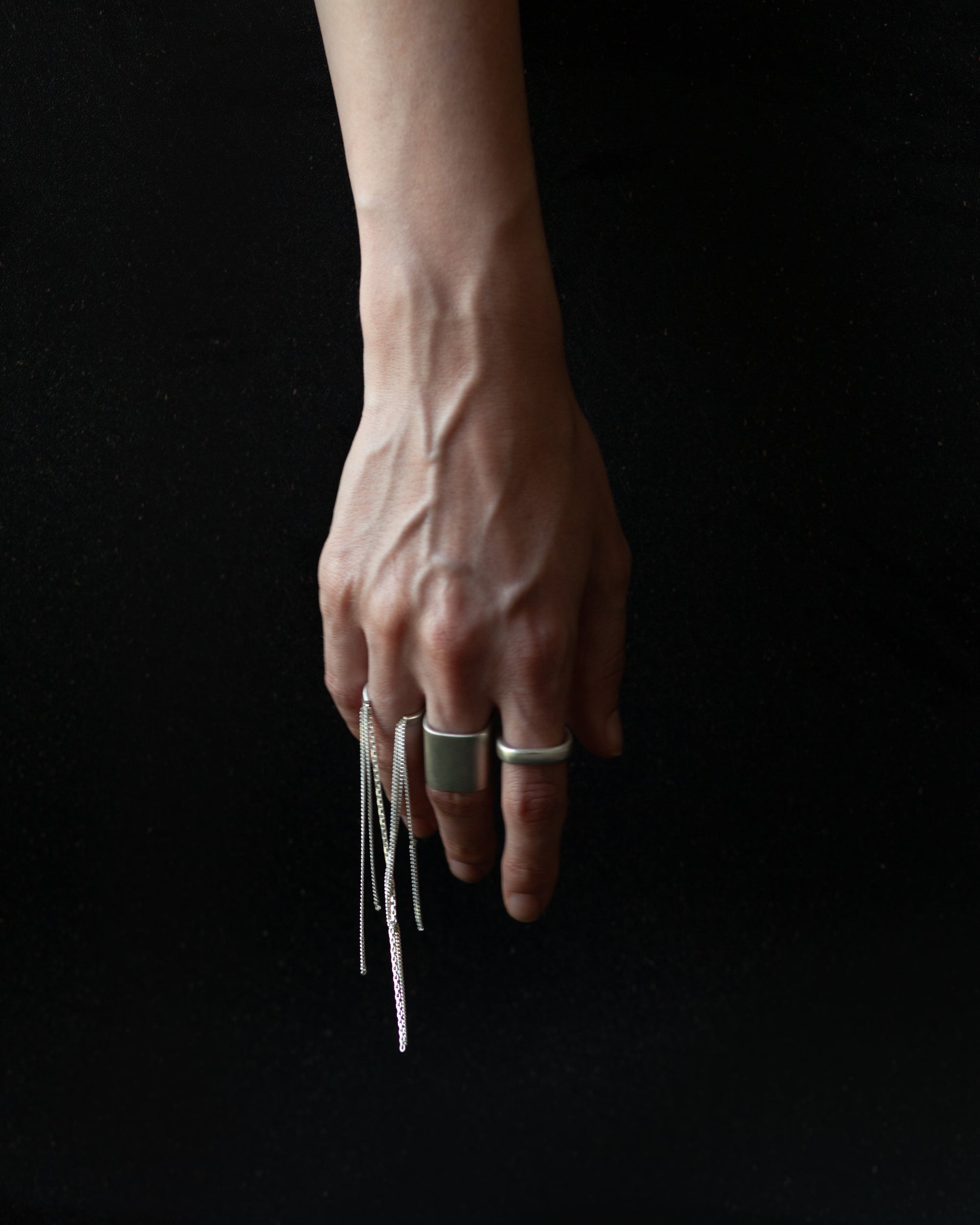 Hand wearing multiple rings with dangling earrings on a black background
