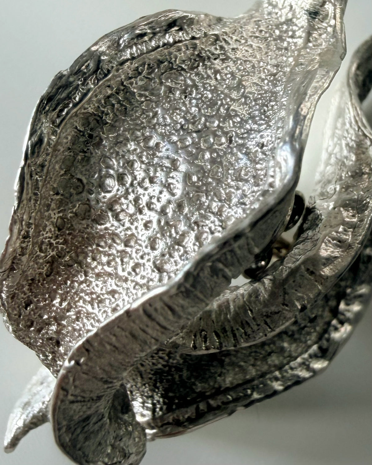 A close-up of a textured silver wave shaped sculptural earrings bubbly surface and layered petals.